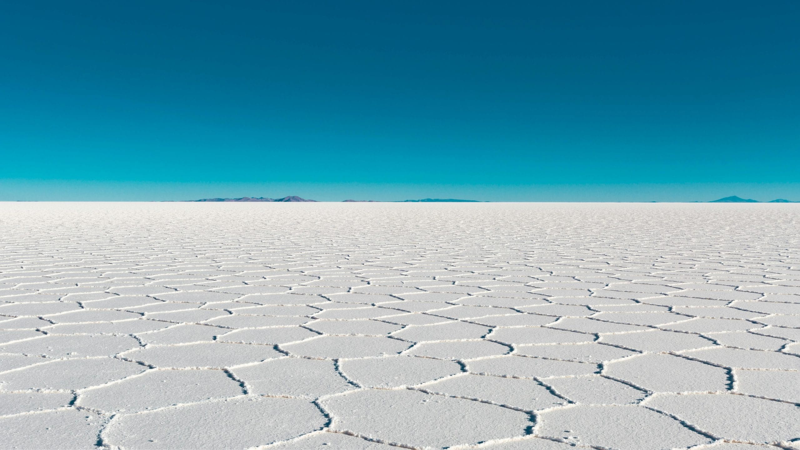 Vast salar with geometric patterns under a clear blue sky in Bolivia's Uyuni.